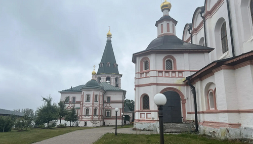 Православный храм с бело-розовыми стенами и золотыми куполами, тропинка и фонари во дворе на фоне пасмурного неба