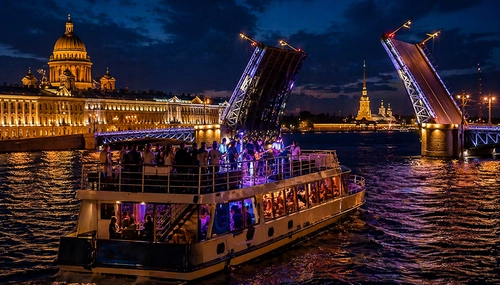 Теплоход с пассажирами проходит под разведённым мостом на Неве ночью; слева Исаакиевский собор, шпиль крепости